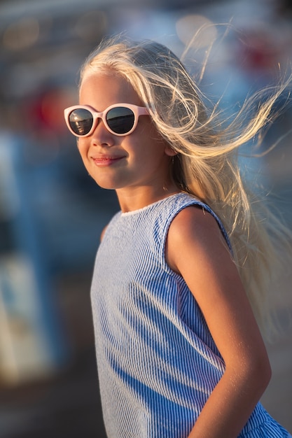 Retrato de una linda niña sonriente con gafas.Una niña en pantalones cortos y una camiseta azul al atardecer junto al mar.Turquía