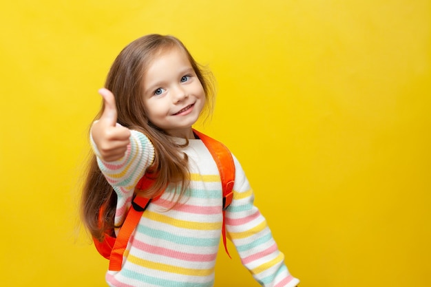 Retrato de una linda niña sonriente con una mochila Europea Regreso a la escuela Thumbs up