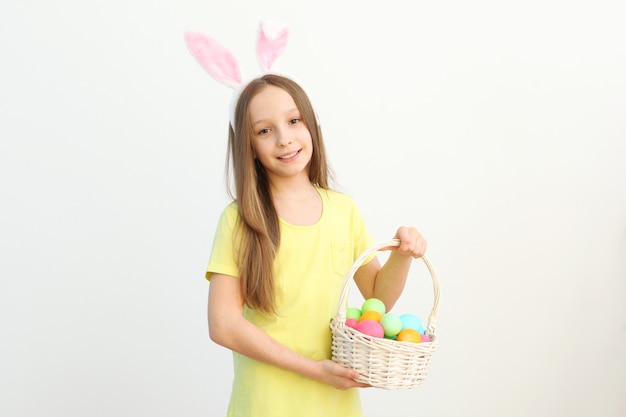 Retrato de una linda niña sonriente con orejas de conejo y huevos de pascua en las manos