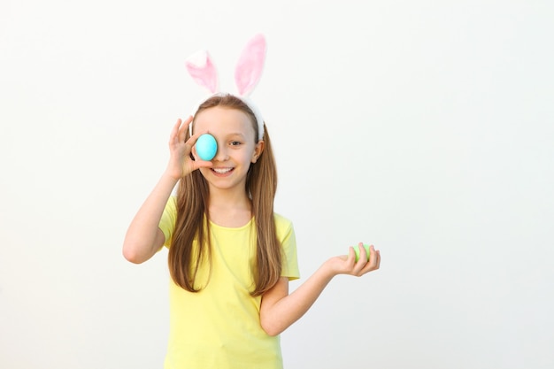 Retrato de una linda niña sonriente con orejas de conejo y huevos de pascua en las manos