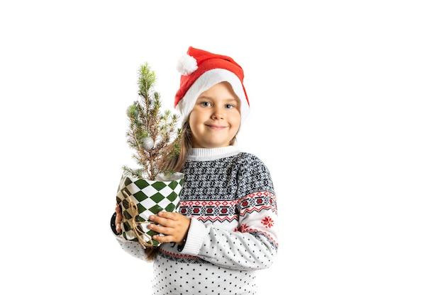 Retrato de una linda niña sonriente en un suéter blanco de navidad con renos y un sombrero de santa claus hol ...