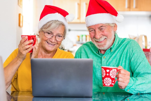 Retrato de una linda pareja de ancianos maduros divirtiéndose y disfrutando el día de Navidad hablando en línea con una computadora portátil en casa con algunos viejos amigos