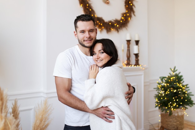 Retrato de linda pareja sonriente enamorada en suéteres acogedores cerca del árbol de Navidad en casa