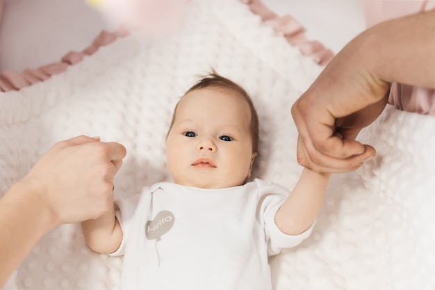 Retrato de un lindo bebé de 6 meses, una niña recién nacida acostada en una cuna y sosteniendo las manos de sus padres