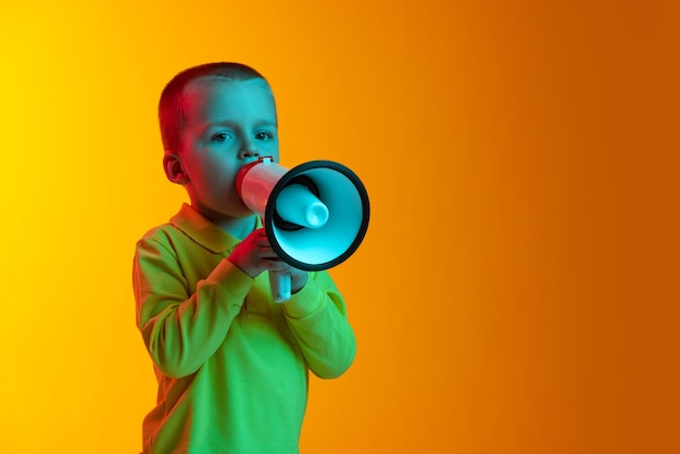 Retrato de un lindo bebé posando gritando en un megáfono aislado sobre fondo amarillo con luz de neón