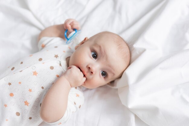 Retrato de un lindo bebé recién nacido con un chupete acostado de espaldas sobre una sábana blanca