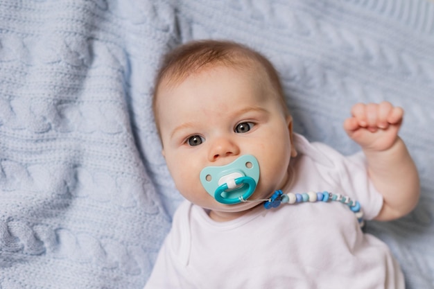 Retrato de un lindo bebé recién nacido con un chupete en la boca acostado boca arriba sobre una manta de punto azul. amamantamiento. concepto de una infancia feliz y maternidad. un niño sano. foto de alta calidad