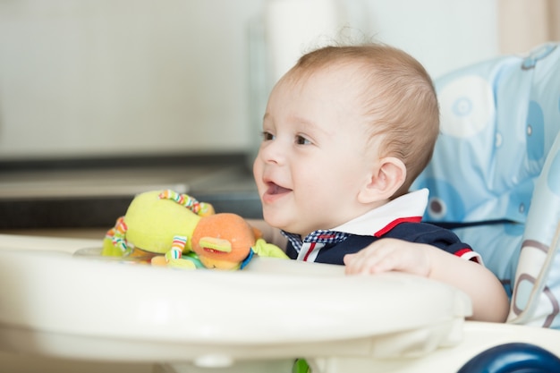 Foto retrato de lindo bebé sonriente sentado en una trona en la cocina