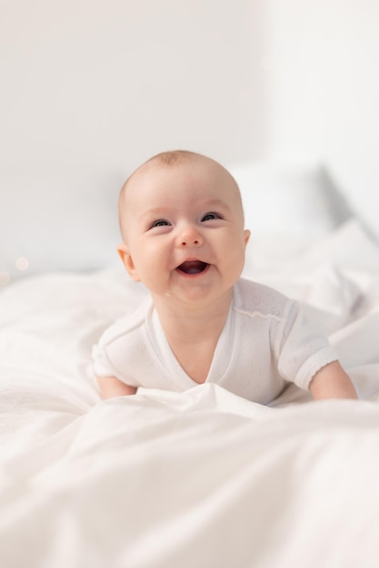 retrato de un lindo bebé con un traje blanco en una cama en casa con sábanas blancas. Bebé recién nacido en casa