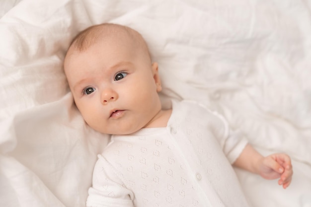 retrato de un lindo bebé con un traje blanco en una cama en casa con sábanas blancas. Bebé recién nacido en casa