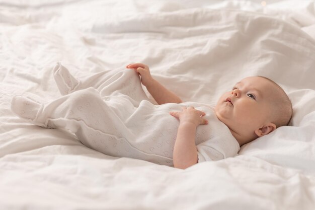 retrato de un lindo bebé con un traje blanco en una cama en casa con sábanas blancas. Bebé recién nacido en casa