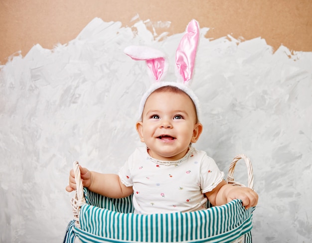 Retrato de un lindo bebé vestido con orejas de conejo de Pascua en una cesta tiene huevo