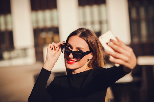 Retrato lindo de una mujer atractiva joven que sostiene un smartphone y que toma un retrato del selfie.