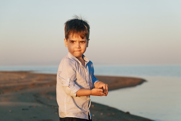 Retrato de un lindo niño de 3 años en la playa en la iluminación del atardecer.