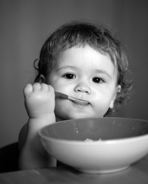Retrato de un lindo niño caucásico con cuchara, hambriento, desordenado, con un plato después de comer puré.