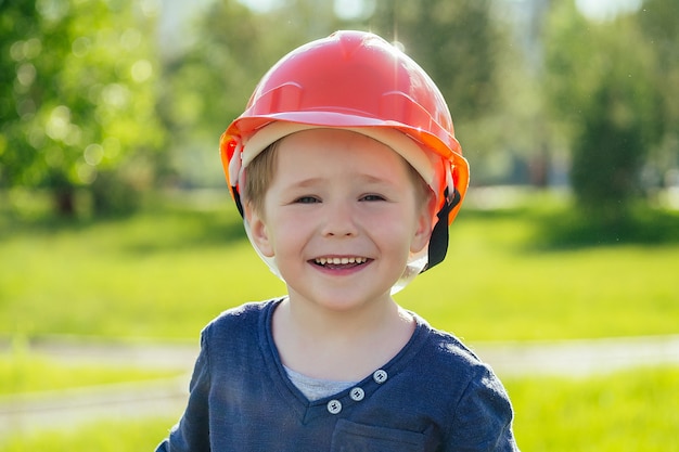 Retrato de lindo niño europeo en un casco de construcción en el parque sobre un fondo de hierba verde y árboles. concepto de orientación profesional