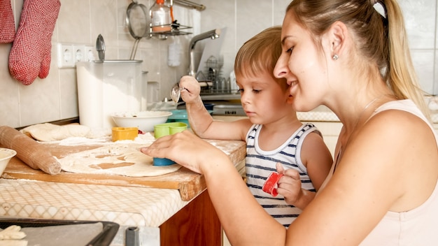 Retrato de lindo niño con joven madre horneando galletas en un molde para hornear en la cocina