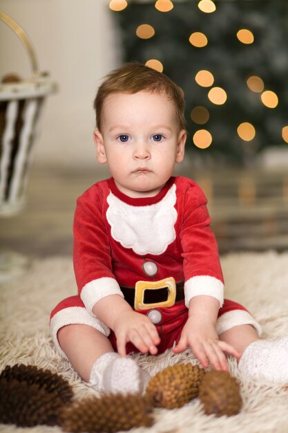 Retrato de un lindo niño jugando en el piso con conos para decorar el árbol de Navidad, cerca del árbol de Navidad y cajas con regalos de Navidad, Feliz Navidad y felices fiestas,