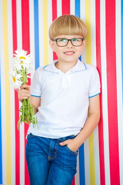 Retrato lindo del niño lindo en colorido. Adorable niño parado cerca de la pared. Niño con un ramo de flores.