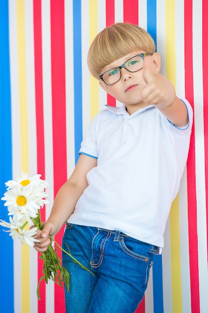 Retrato lindo del niño lindo en colorido. Adorable niño parado cerca de la pared. Niño con un ramo de flores.