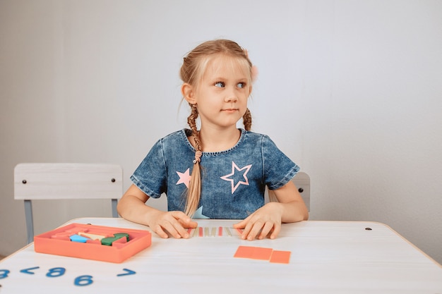 Retrato de un lindo niño lindo sentado en una mesa blanca y resolviendo rompecabezas y problemas intelectuales. Desarrollo infantil. Concepto de mente. foto con ruido