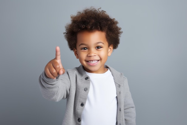 Retrato de un lindo niño mostrando los pulgares hacia arriba contra el fondo gris