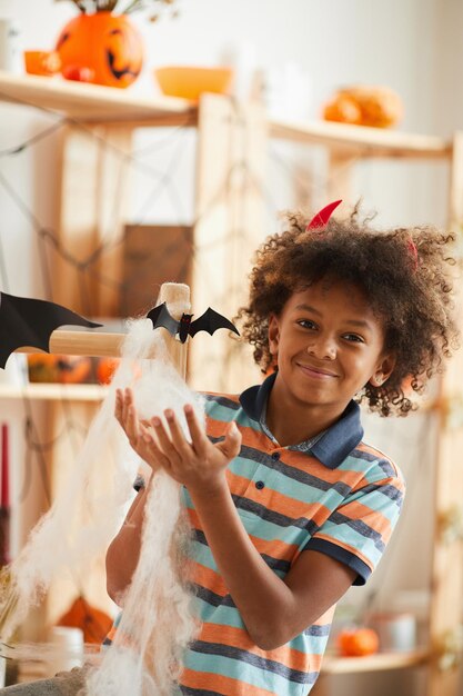 Retrato de un lindo niño negro sonriente sosteniendo algodón envuelto alrededor de estantes de madera que se divierte en hal