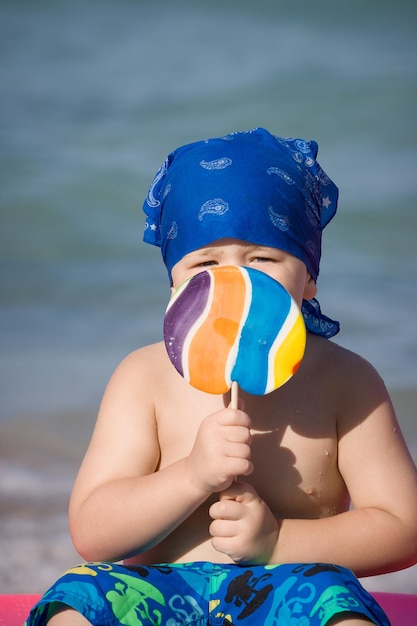 Foto retrato de un lindo niño pequeño con un gran llolipop colorido en la playa del mar