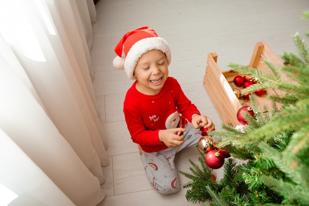 Retrato de un lindo niño en pijama rojo decorando un árbol de Navidad concepto de año nuevo de invierno