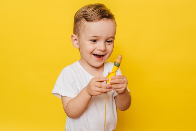 Retrato de un lindo niño riendo en amarillo con un juguete en sus manos