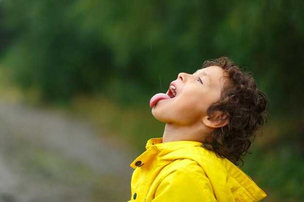 retrato de un lindo niño rizado atrapando las gotas de lluvia por su lengua