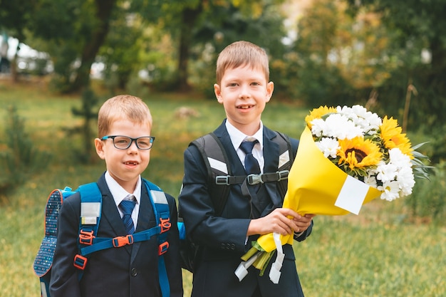 Retrato de lindo niño de siete años de primer grado con ramo de flores con hermano