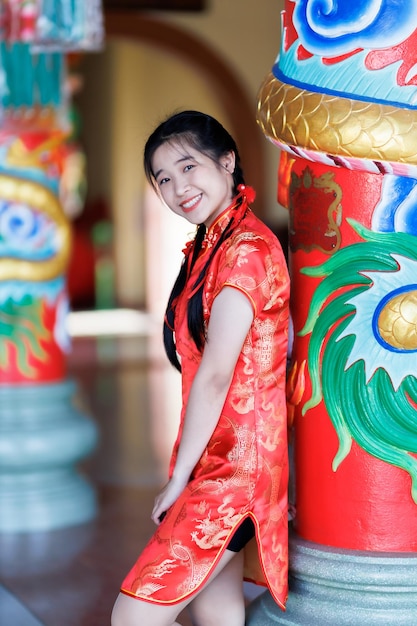 Retrato lindos sorrisos fofos jovem asiática vestindo decoração cheongsam chinesa tradicional vermelha e segurando um Fanning chinês para o Festival do Ano Novo Chinês no santuário chinês na Tailândia