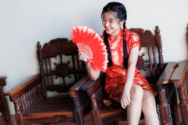 Retrato lindos sorrisos fofos jovem asiática vestindo decoração cheongsam chinesa tradicional vermelha e segurando um fanning chinês para o festival do ano novo chinês no santuário chinês na tailândia