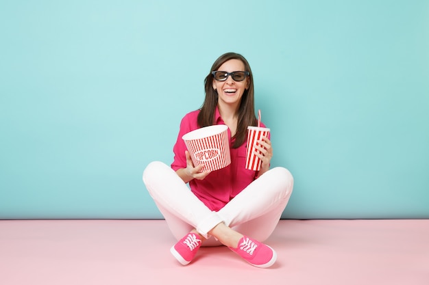 Retrato de longitud completa mujer divertida en camisa rosa, pantalón blanco sentado en el piso viendo una película