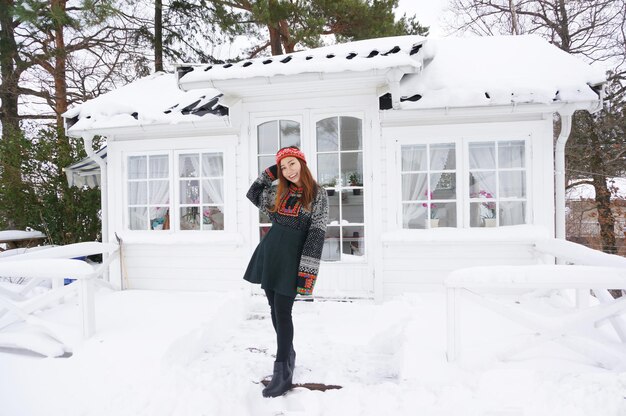 Foto retrato de longitud completa de una mujer joven de pie en una casa cubierta de nieve