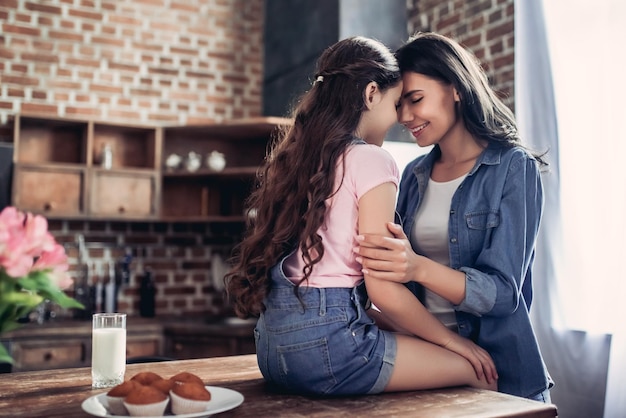 Retrato de madre abrazando a su hija sentada en la mesa de la cocina