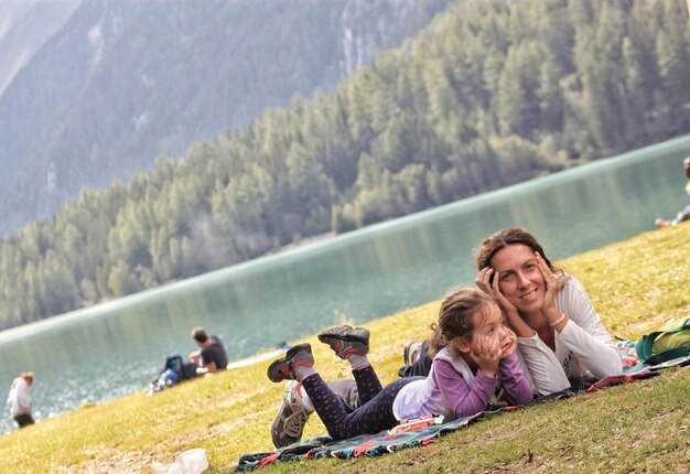 Retrato de una madre acostada con su hija en la orilla del lago contra los árboles