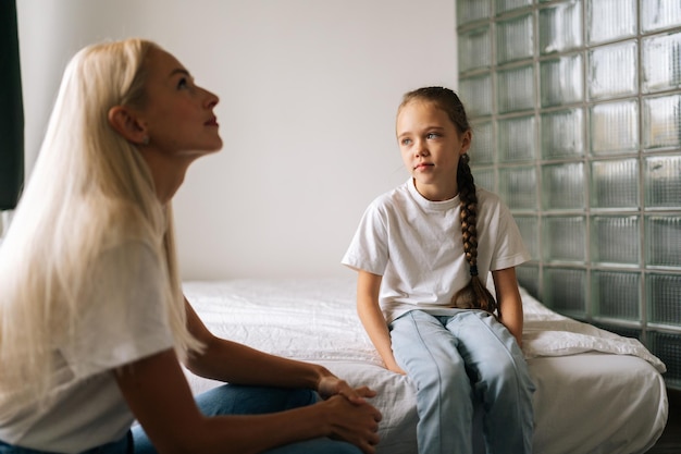 Retrato de una madre adulta joven rubia y un niño lindo disfrutan hablando relajándose sentados en la cama en un dormitorio claro