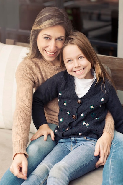 Retrato de una madre alegre sentada con su hija en el sofá