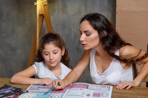 Retrato de una madre ayudando a su pequeña hija dulce y linda a hacer sus deberes en el interior feliz fa ...