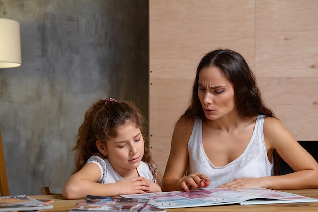 Retrato de una madre ayudando a su pequeña hija dulce y linda a hacer sus deberes en el interior feliz fa ...
