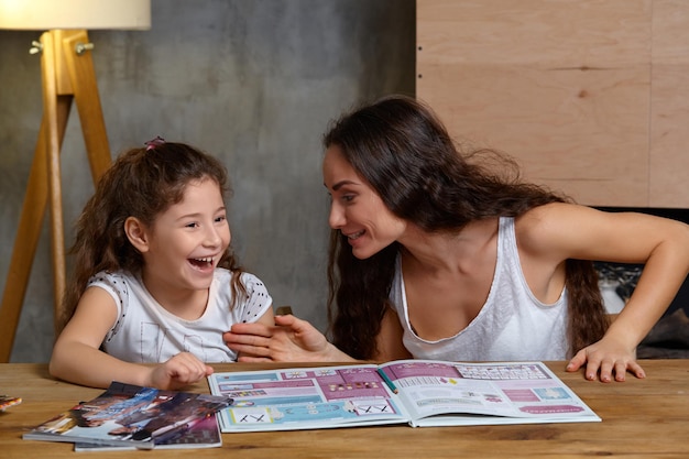 Retrato de una madre ayudando a su pequeña hija dulce y linda a hacer sus deberes en el interior feliz fa ...