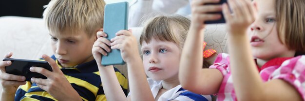 Retrato de una madre divertida que cuida a los niños niños concentrados que sostienen teléfonos inteligentes y