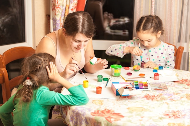 Retrato de madre con dos hijas pintando huevos de pascua