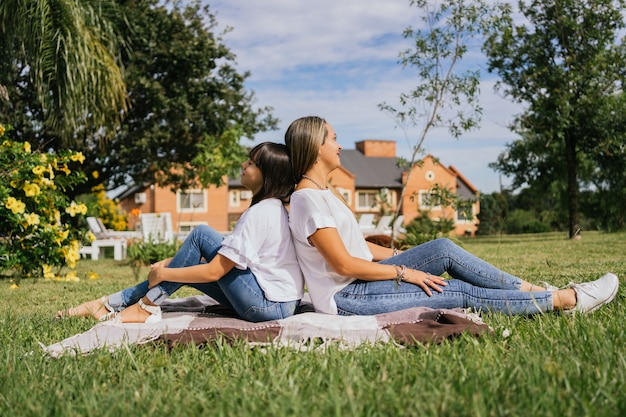 Retrato de madre e hija sentadas espalda con espalda al aire libre.