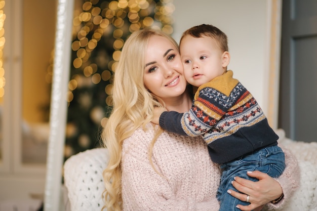 Retrato de madre e hijo sentados en un autocar en casa cerca del árbol de Navidad, todos están sonriendo. Familia navideña. Felicidad.