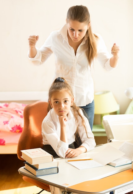 Retrato de madre enojada jura por hija haciendo los deberes