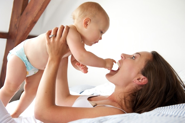 Retrato de una madre feliz y bebé jugando en la cama