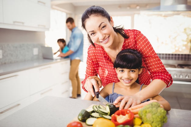 Retrato de madre feliz enseñando a hija a cortar verduras